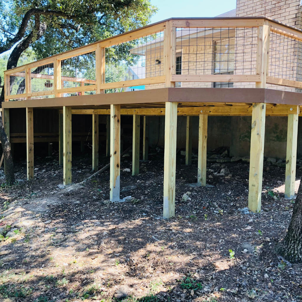 Elevated wooden deck by Alamo City Decks and Patios surrounded by lush trees, providing a spacious outdoor living area.